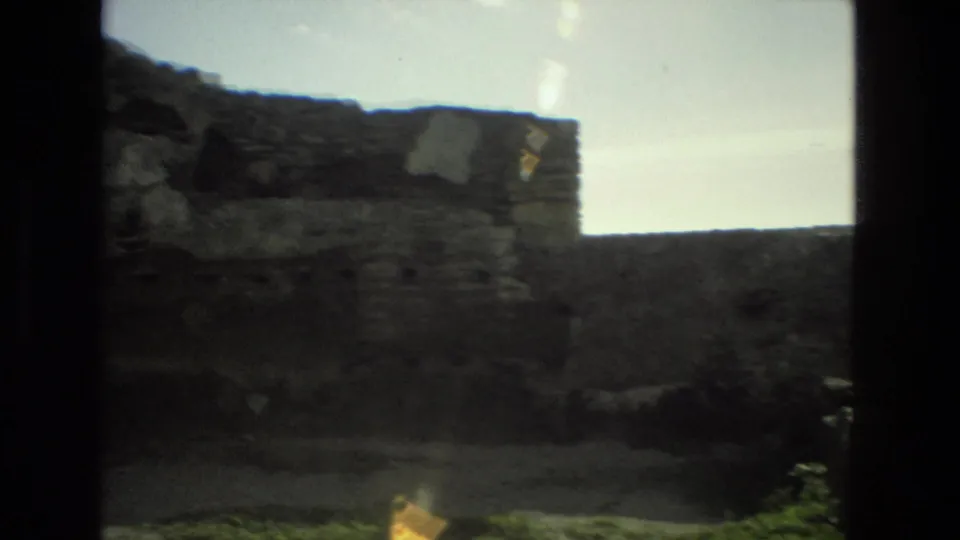 Handheld 8mm view in Granada showing worn stone wall sections, rubble-like masonry, and bright sky.