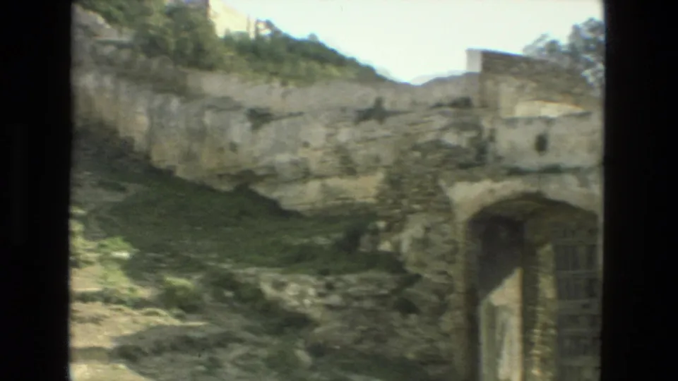 Handheld Granada 8mm frame showing a ruin interior area with broken stone walls, greenery, and an arched doorway.