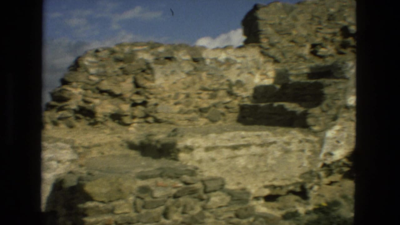 Weathered stone ruins and rocky ground under a partly cloudy blue sky.