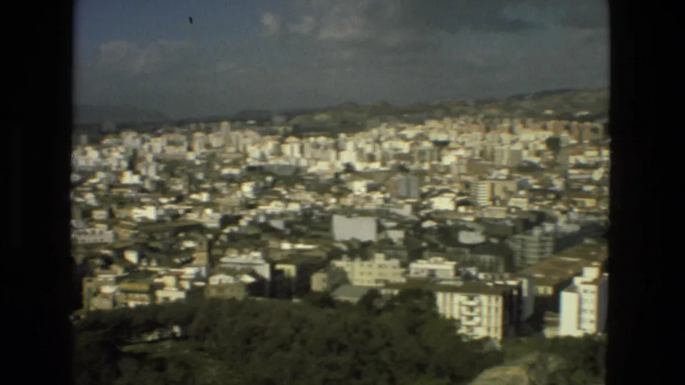 1978 8mm view over Granada, Spain, showing a broad cityscape with white buildings, wooded foreground, distant hills, and film-frame edges.