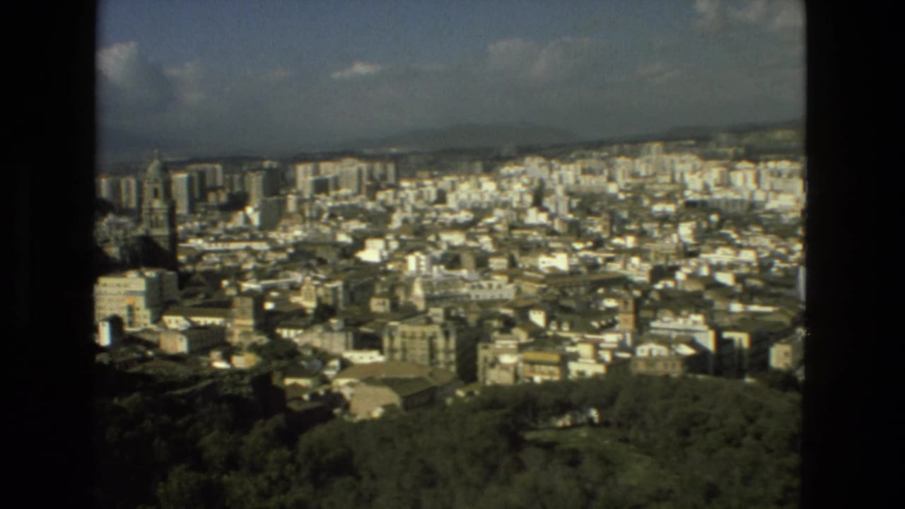 1978 8mm Granada city view with a prominent cathedral tower rising among apartment blocks, wooded foreground, hills, and sky.