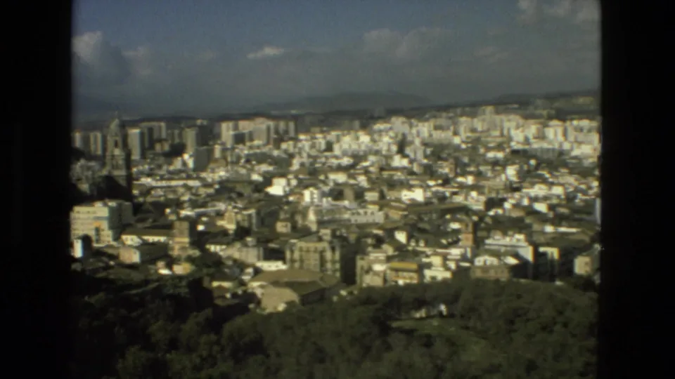 1978 8mm Granada city view with a prominent cathedral tower rising among apartment blocks, wooded foreground, hills, and sky.