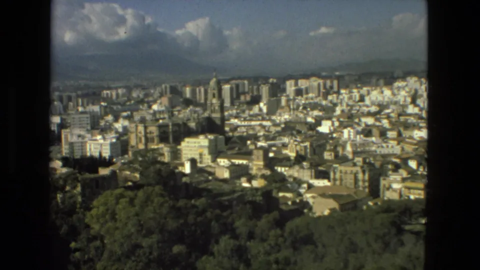 1978 8mm frame of Granada with the cathedral tower near center, surrounding high-rises, dense white buildings, trees, and mountains behind.