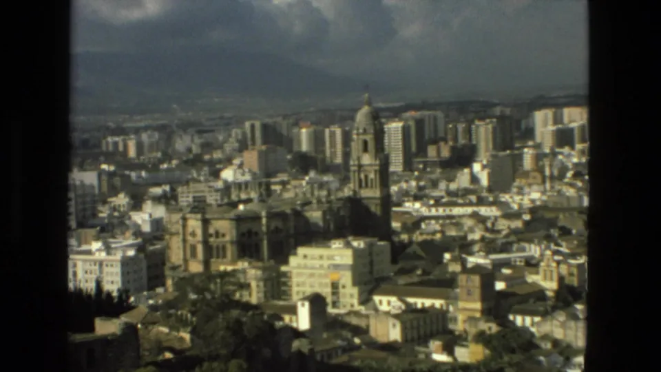 1978 8mm Granada view zoomed toward the cathedral tower, with dense city buildings, wooded lower edge, hazy hills, and warm film color.