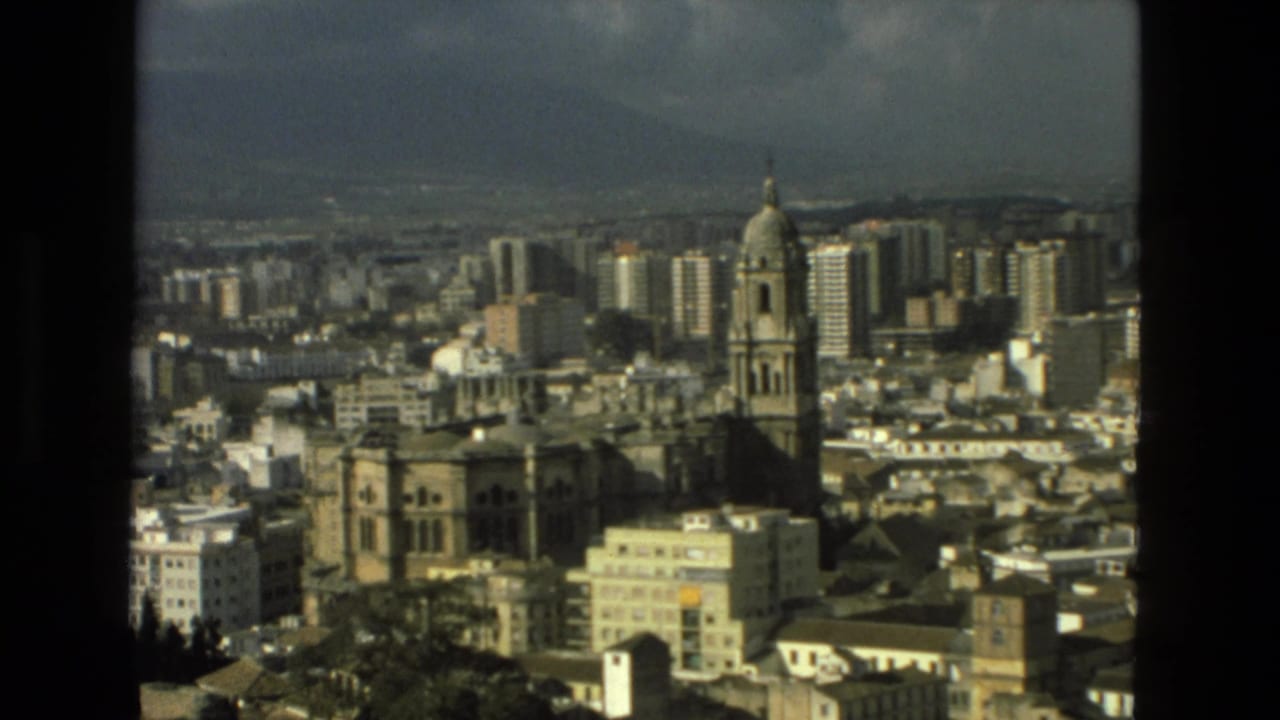 1978 8mm view over Granada, Spain, showing a cathedral-like landmark, dense urban buildings, distant hills, and dark film borders.