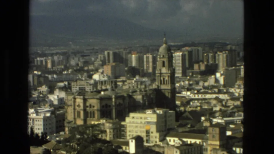 1978 8mm view over Granada, Spain, showing a cathedral-like landmark, dense urban buildings, distant hills, and dark film borders.