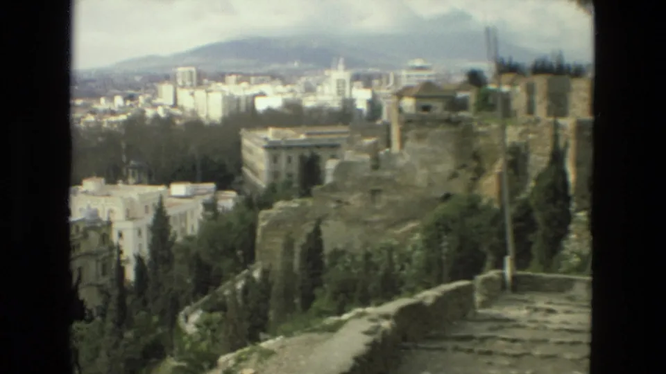 Granada overlook with old stonework, trees, a pale civic-looking building, dense city blocks, and hills softened by 8mm film grain.