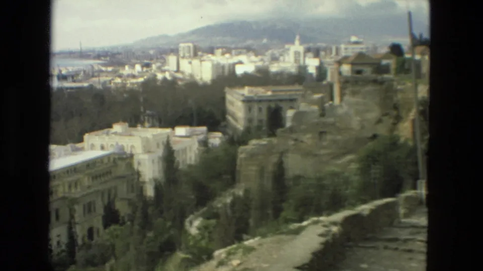 1978 8mm travel view in Granada, Spain, looking past historic stone ruins toward trees, city buildings, water, and mountains.