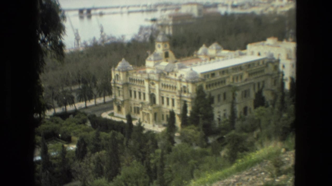 Final 1978 Granada frame shows the domed building and clock tower surrounded by greenery, with a water body and port-like cranes in the distance.