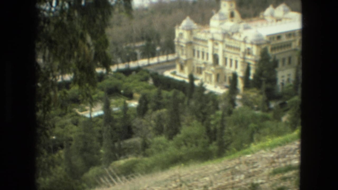 Palace and gardens viewed through dark vertical film-frame edges.
