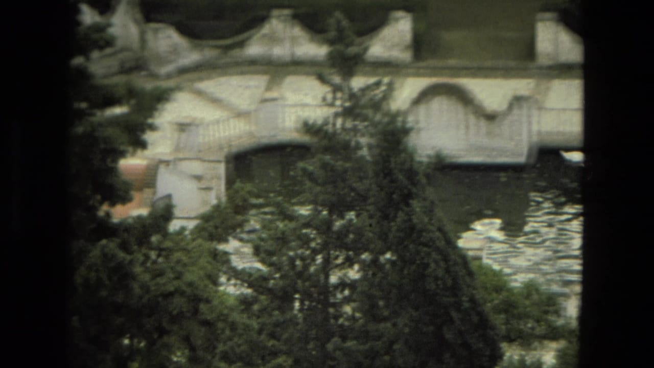 1978 8mm Granada garden view with a white ornamental bridge, reflective water, and dense trees framing the scene.