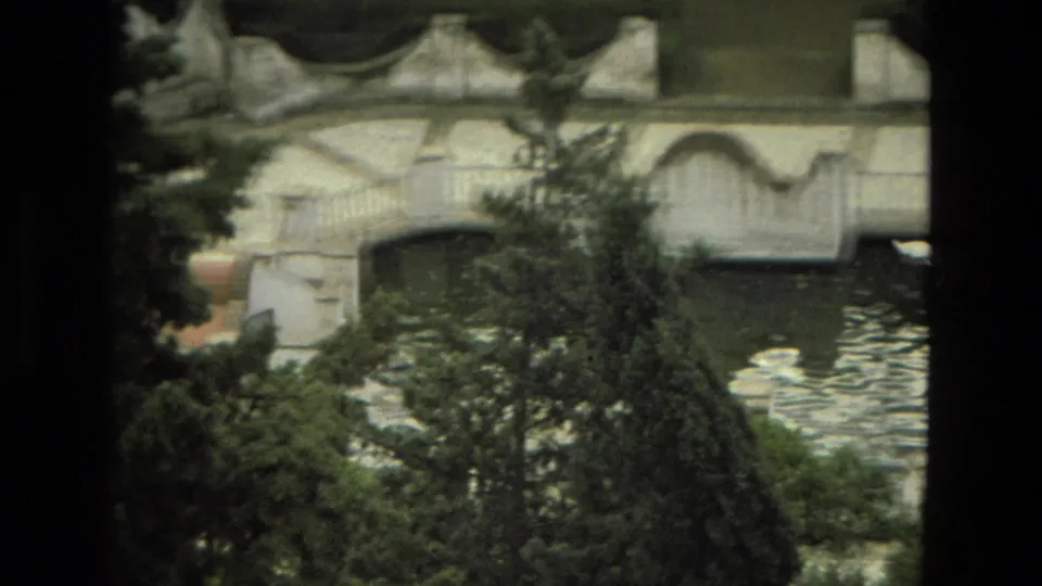 1978 8mm Granada garden view with a white ornamental bridge, reflective water, and dense trees framing the scene.