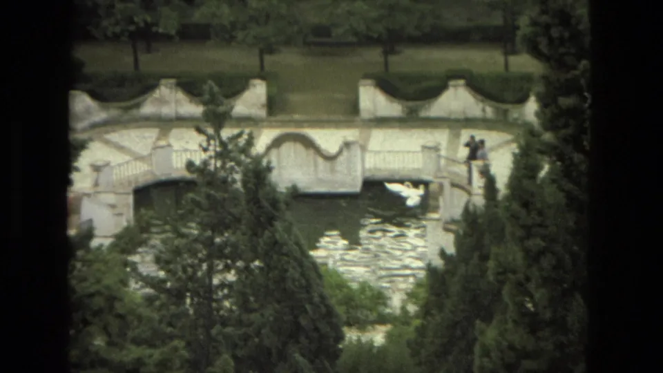 1978 Granada garden footage showing the white ornamental bridge, water below, distant visitors, and a white bird crossing the frame.