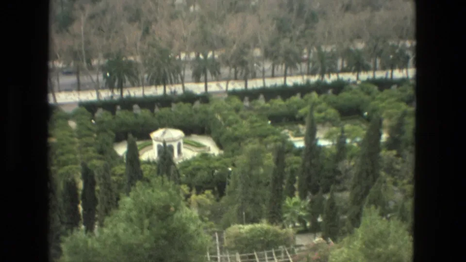 1978 Granada travel footage frame looking down at a white pavilion amid cypress trees, hedges, and layered urban greenery.