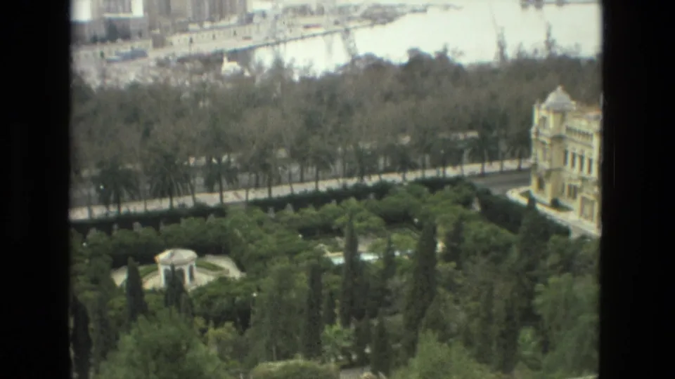 Wide 1978 Granada frame showing the garden pavilion below, a tree-lined road, a pale building, and a bright waterfront or paved area beyond.
