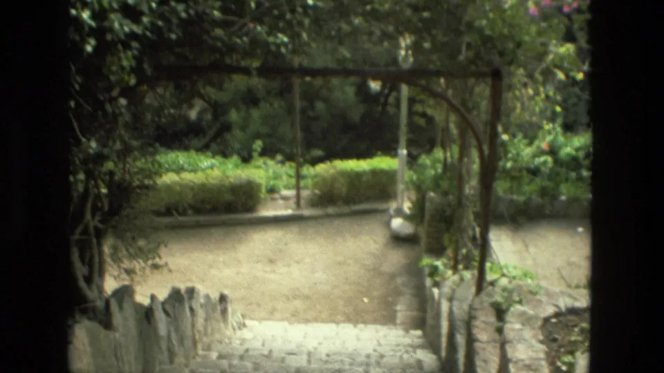 1978 8mm Granada garden view with a shaded arch, gravel path, low hedges, and pale stone steps in the foreground.