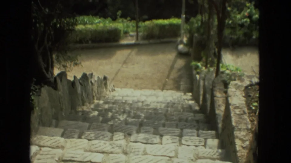Stone steps in a Granada garden descend toward a gravel path, bordered by rough rock walls and shaded greenery.