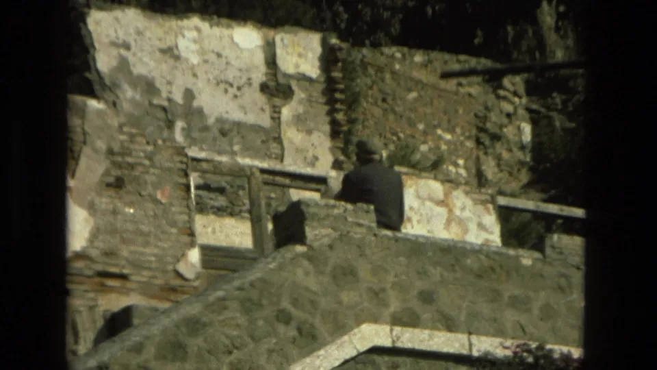 1978 Granada 8mm frame showing weathered stone steps, patchy walls, plants, and a distant dark-clothed person on the structure.