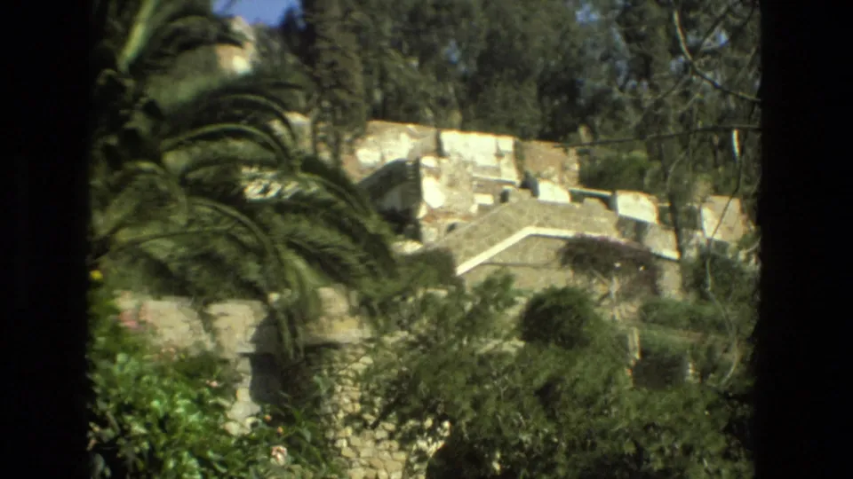 Granada 1978 frame with palm fronds, shrubs, trees, and layered stone garden walls on a hillside.