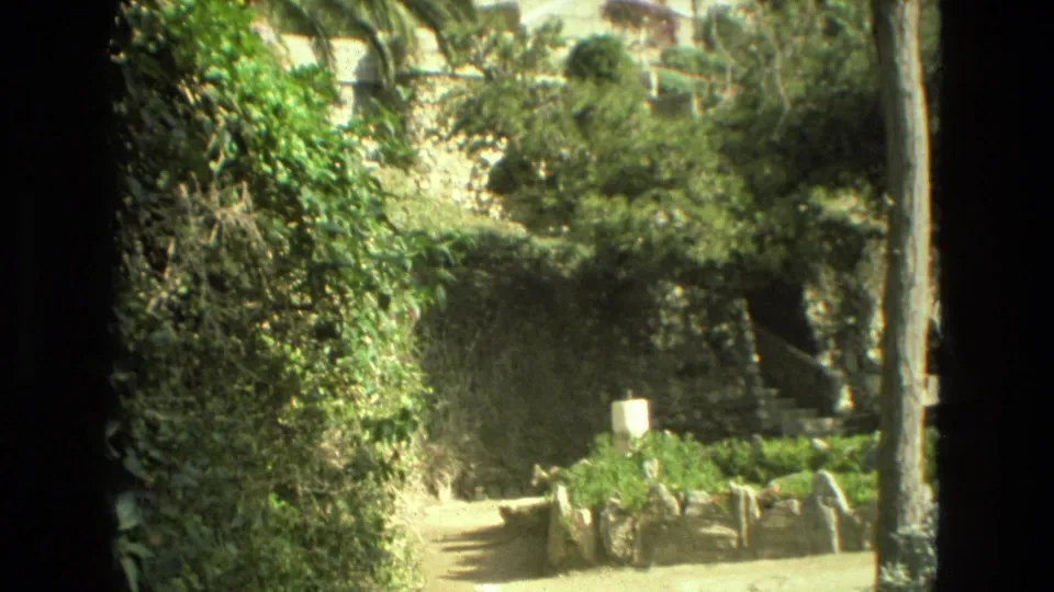 Granada 1978 garden view with a winding dirt path, low stone edging, shrubs, trees, and terraced walls above.
