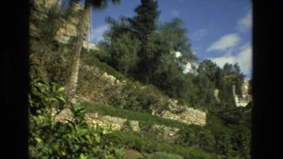 1978 Granada home-movie view across sloped garden terraces, stone walls, dense shrubs, trees, and blue sky.