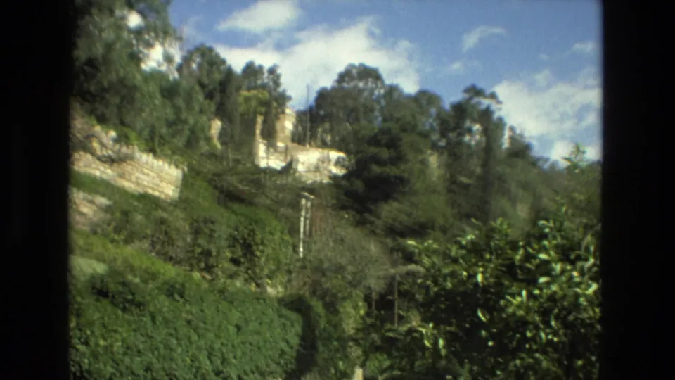 1978 Granada home-movie frame showing a green hillside garden, stone retaining walls, trees, sky, and distant buildings through a window-like divider.