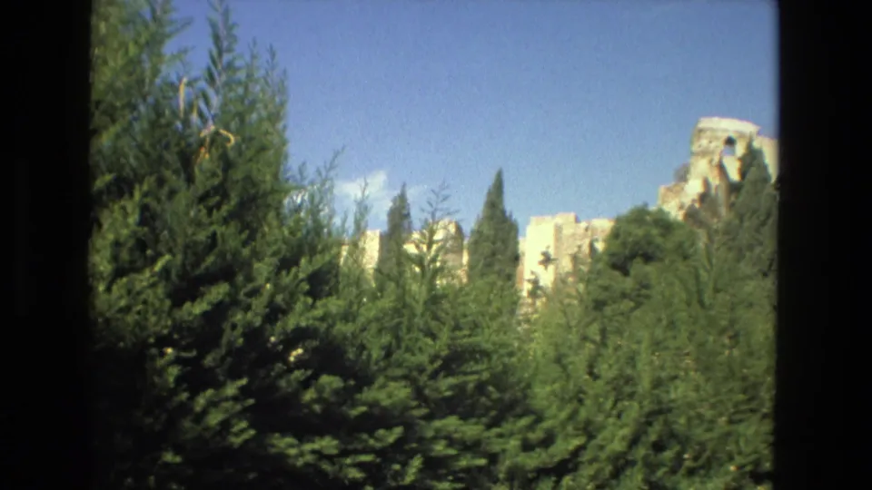 Distant stone ruins in Granada appear beyond evergreen trees in 1978 8mm travel footage.