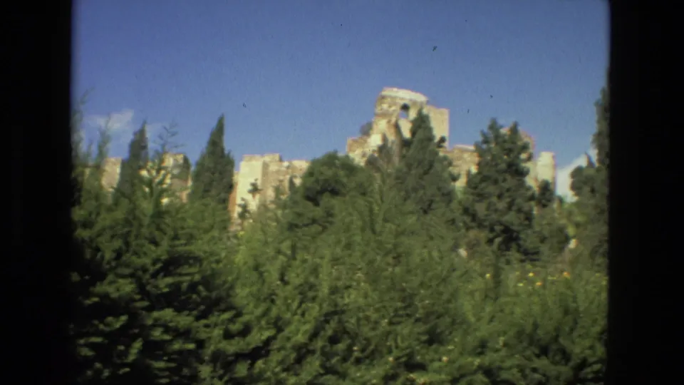A visitor-shot 1978 Granada view frames pale stone ruins behind dark green treetops and clear sky.