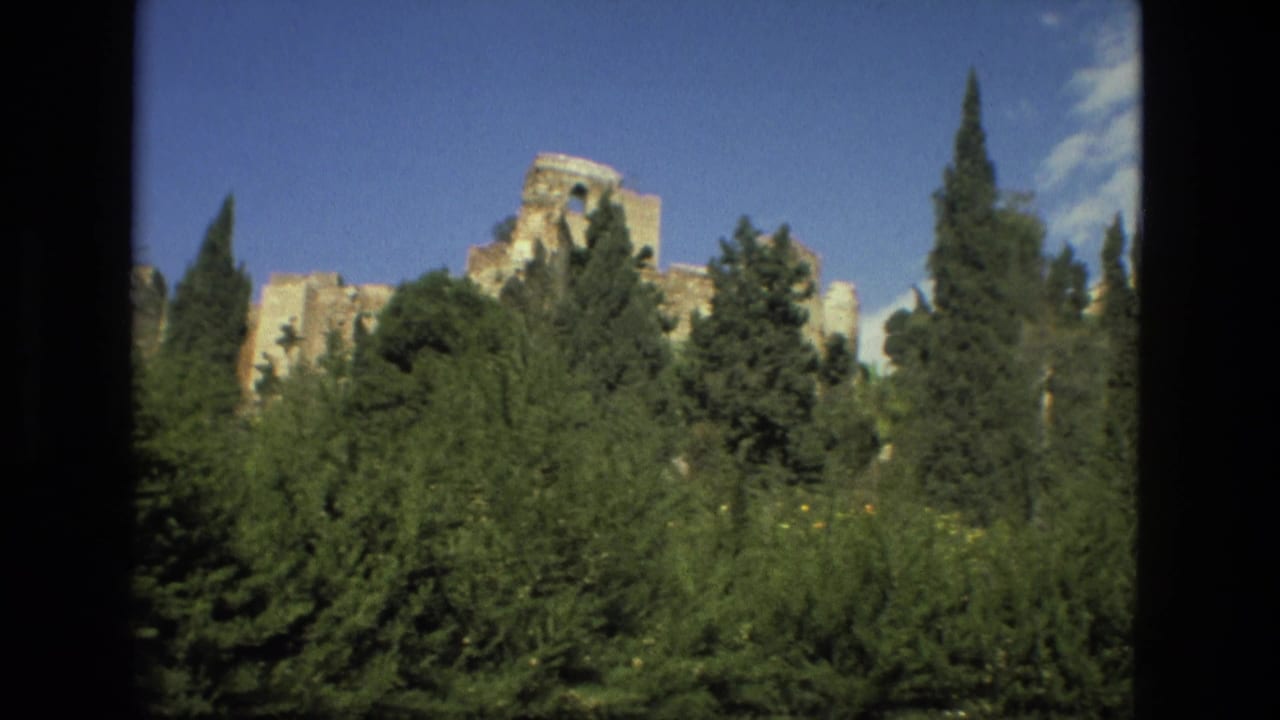 1978 8mm Granada travel frame showing cypress trees and dense greenery below pale historic ruins under a bright sky.