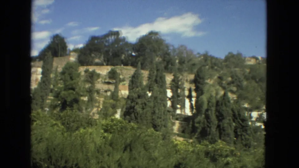 Final 8mm Granada frame showing hillside greenery around pale ruins, with soft focus and bright daylight.