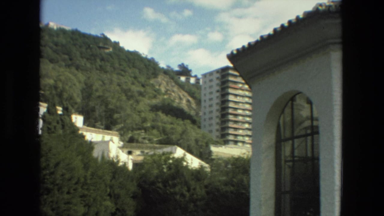Hillside greenery, white buildings, and a tall apartment block seen past dark window framing.