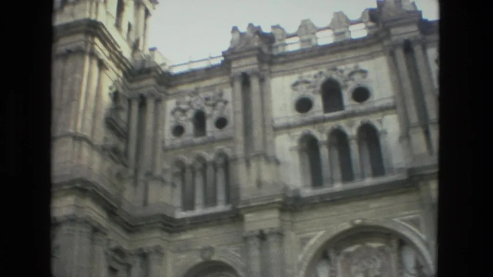 Visitor-shot 8mm frame of the Granada church exterior, showing the upper facade corner, arched windows, and carved stonework.