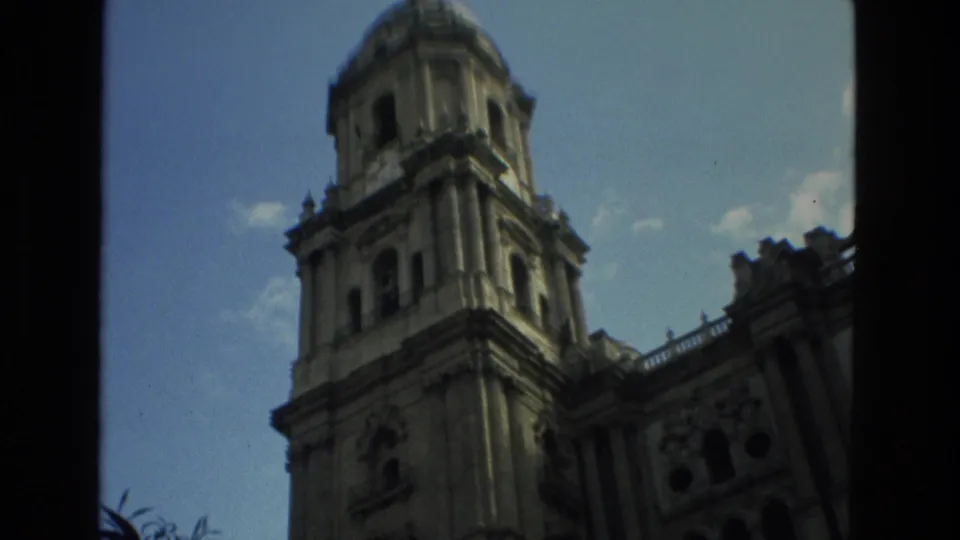 1978 Granada 8mm frame looking up at a church tower, with deep foreground shadow and pale blue sky visible around the stonework.