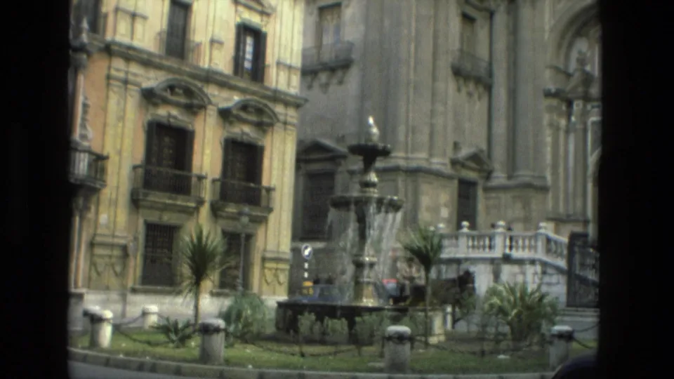 1978 Granada exterior with a tiered fountain, planted square, balconies, and cathedral steps in the background.
