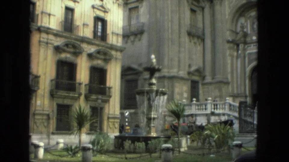 Granada cathedral square with fountain, iron balconies, greenery, and a stone entrance visible on 8mm film.
