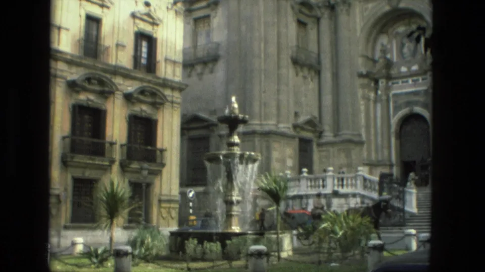 1978 Granada home-movie frame showing an ornate historic facade, plaza fountain, balconies, plants, and a horse carriage near stone steps.