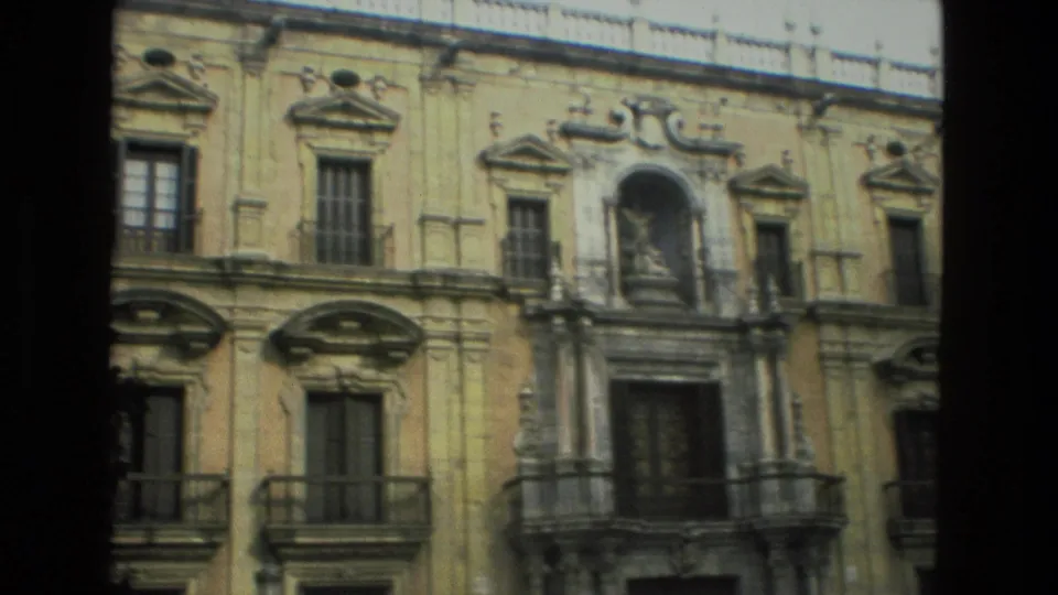 1978 Granada home-movie view of an ornate upper facade with carved stonework, balconies, shuttered windows, an arched niche, and roof railing.