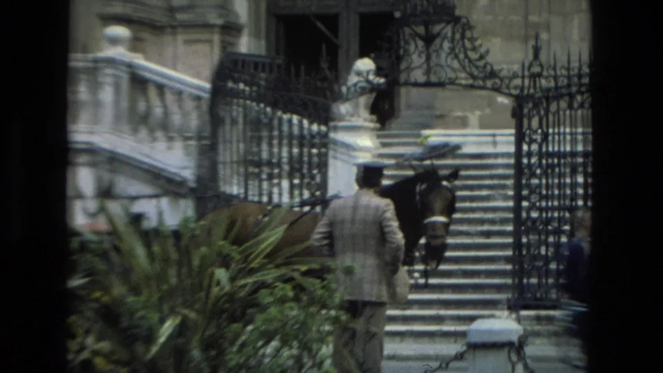 1978 Granada frame showing a suited man in a hat beside a horse and carriage at iron gates, with stone stairs, railings, plants, and a building entrance.
