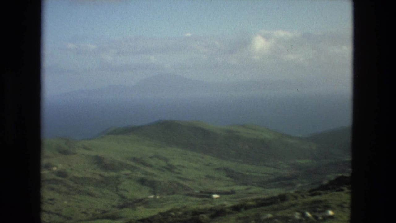 Green hills and valleys under a hazy sky with distant water on the horizon.