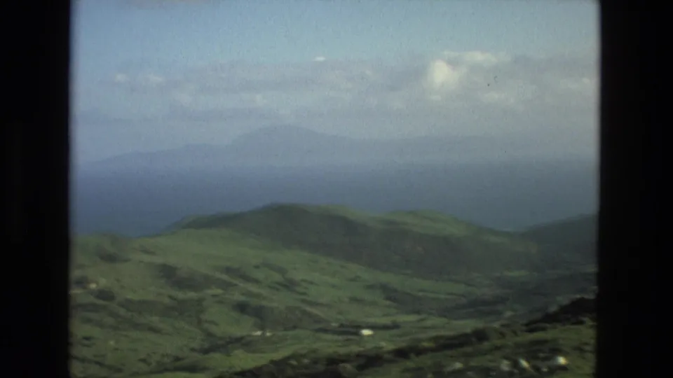 1978 8mm home-movie view near Granada, Spain, looking across green hills toward hazy mountains and distant water.