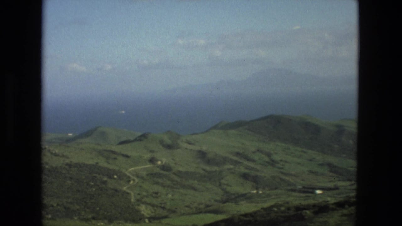 8mm view from the Granada area showing green hill country, pale roads, hazy mountains, and distant sea or water.