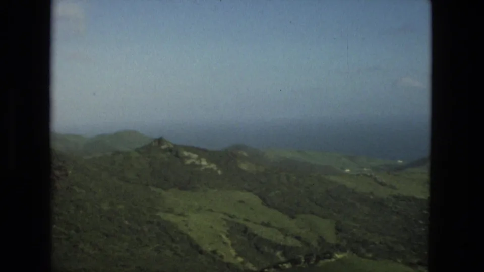 1978 8mm frame near Granada showing rugged green hills, darker wooded areas, distant water, and a hazy horizon.