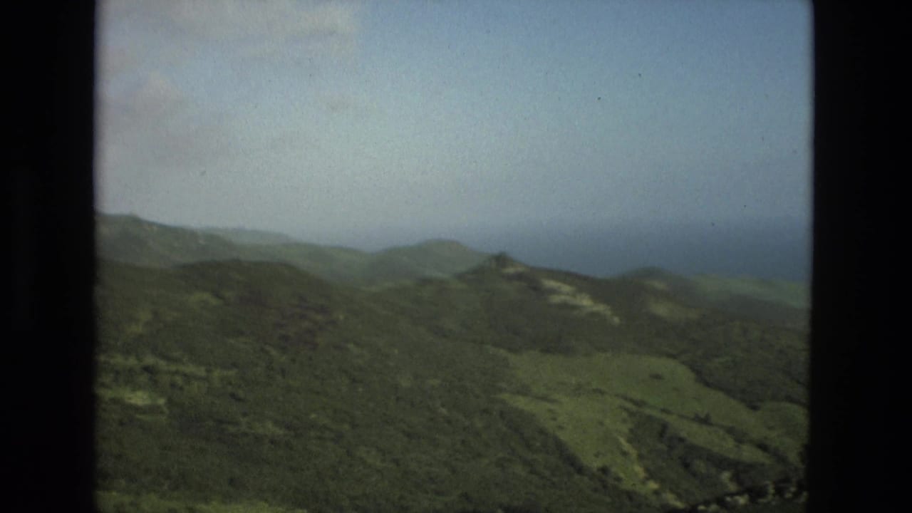 Green mountain ridges beneath a hazy sky, seen from an elevated viewpoint.