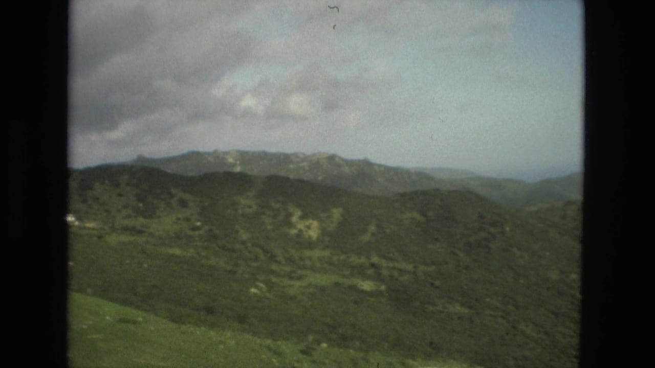 1978 Granada mountain landscape with layered green slopes and a cloud bank over distant ridges.