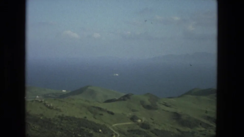 1978 8mm Granada, Spain travel footage showing rolling green hills, hazy sky, and distant water through a dark framed edge.