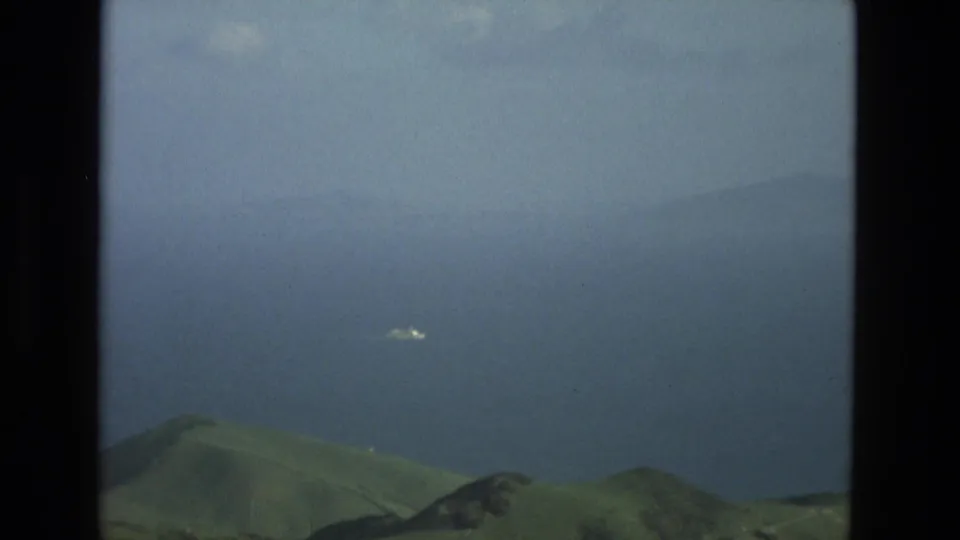 1978 8mm Granada, Spain landscape frame with hillside foreground, distant blue water, soft haze, and heavy dark framing.
