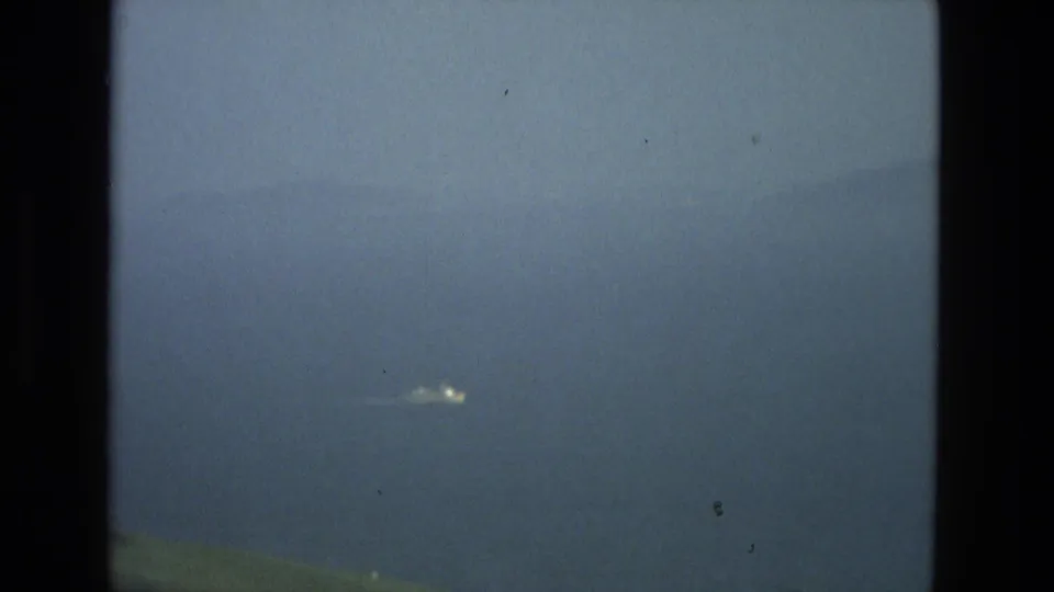 1978 8mm Granada, Spain travel view with hazy blue water, low hillside, dark frame borders, and a small bright distant object.
