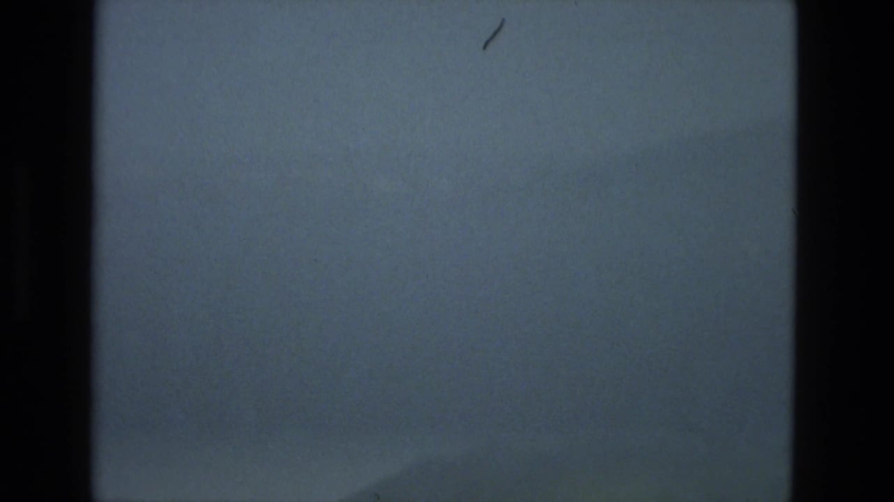 Mostly empty blue-gray sky with scratches, grain, and dark film edges.