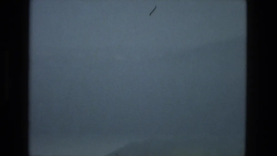 A mostly empty blue-gray sky frame from the same 1978 Granada 8mm clip shows grain, scratches, and dark film edges, with no clear object visible.