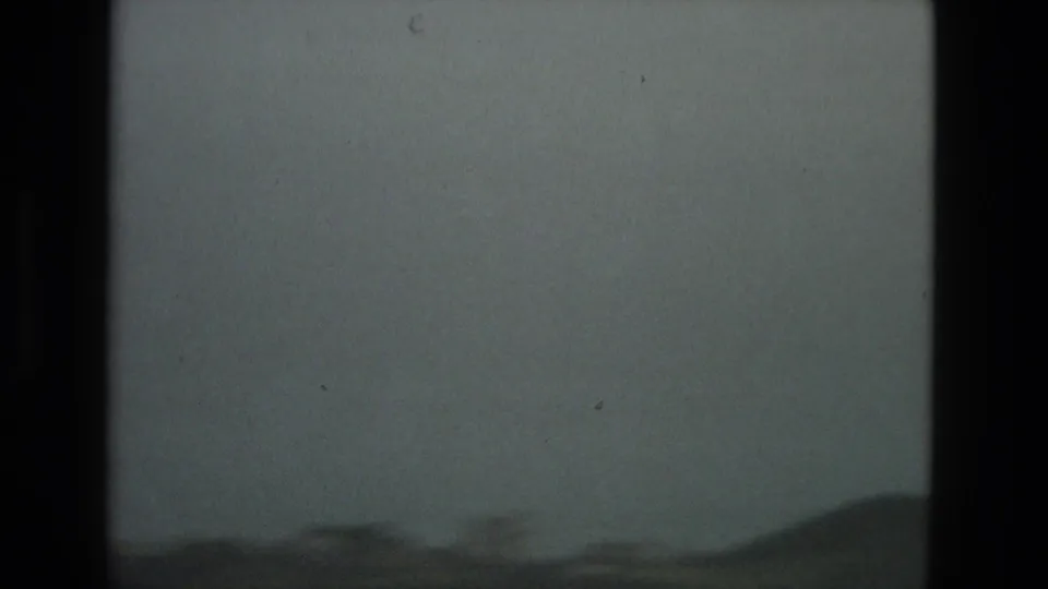 The final frame shows a hazy blue-gray sky above a low dark horizon in the Granada 1978 8mm footage, with grain, dust, and frame-edge artifacts visible.